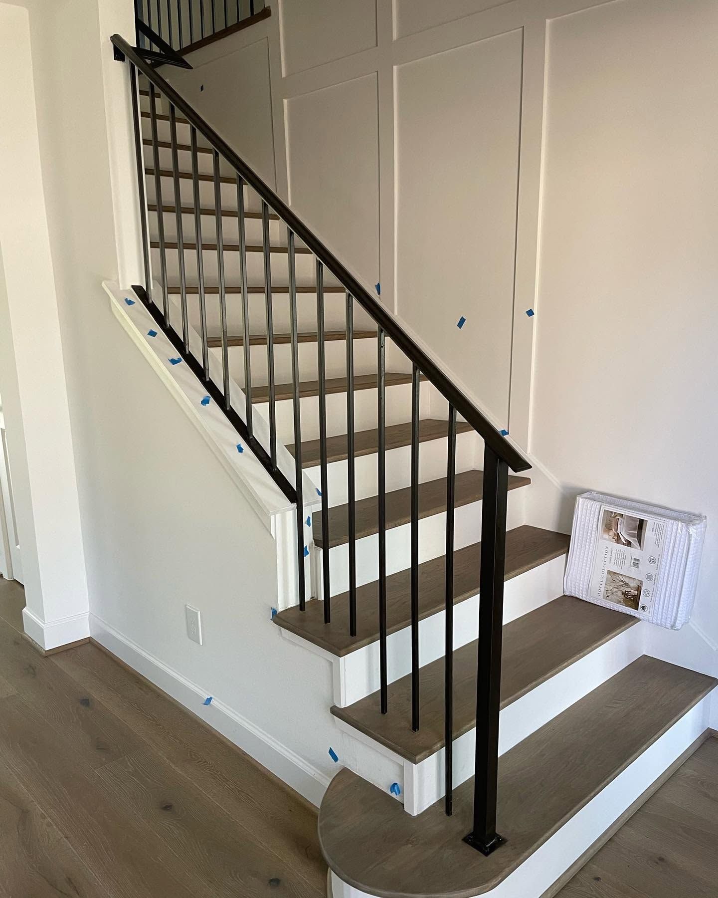 Interior staircase with dark railings and light walls, leading to an upper floor beside a hallway.