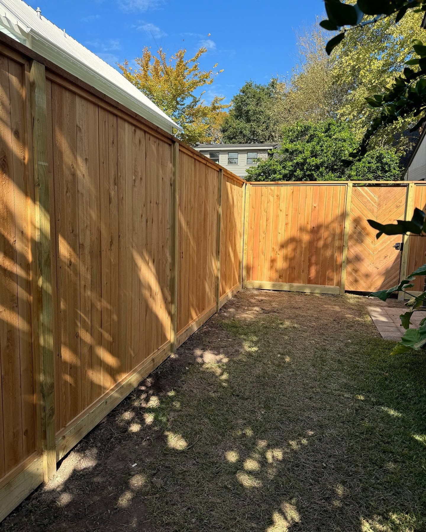 Wooden fence-lined side yard with gravel ground and sunlight shadows, ending at a gate.