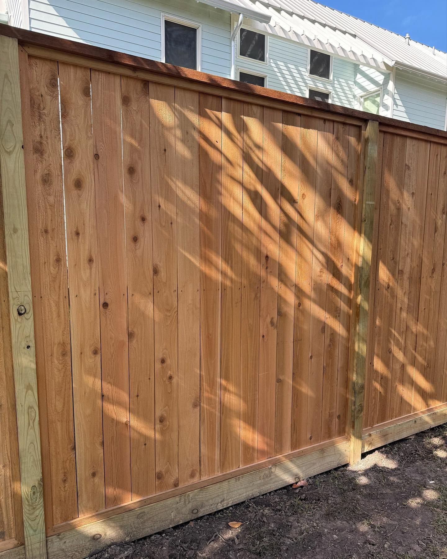 Wooden backyard privacy fence with diagonal sunlight and a house visible above it
