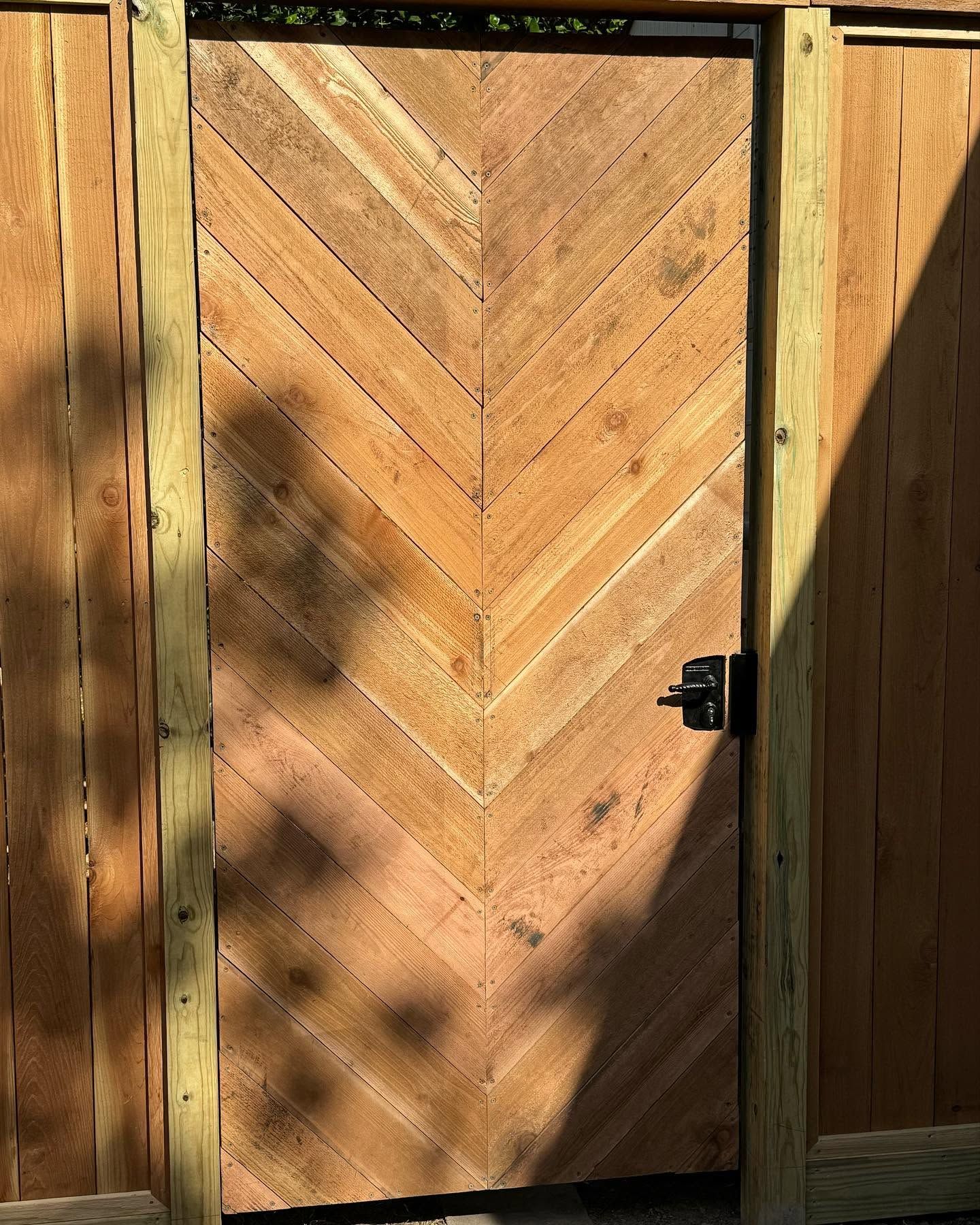 Wooden chevron-pattern door with black handle in a sunlit fence or shed wall
