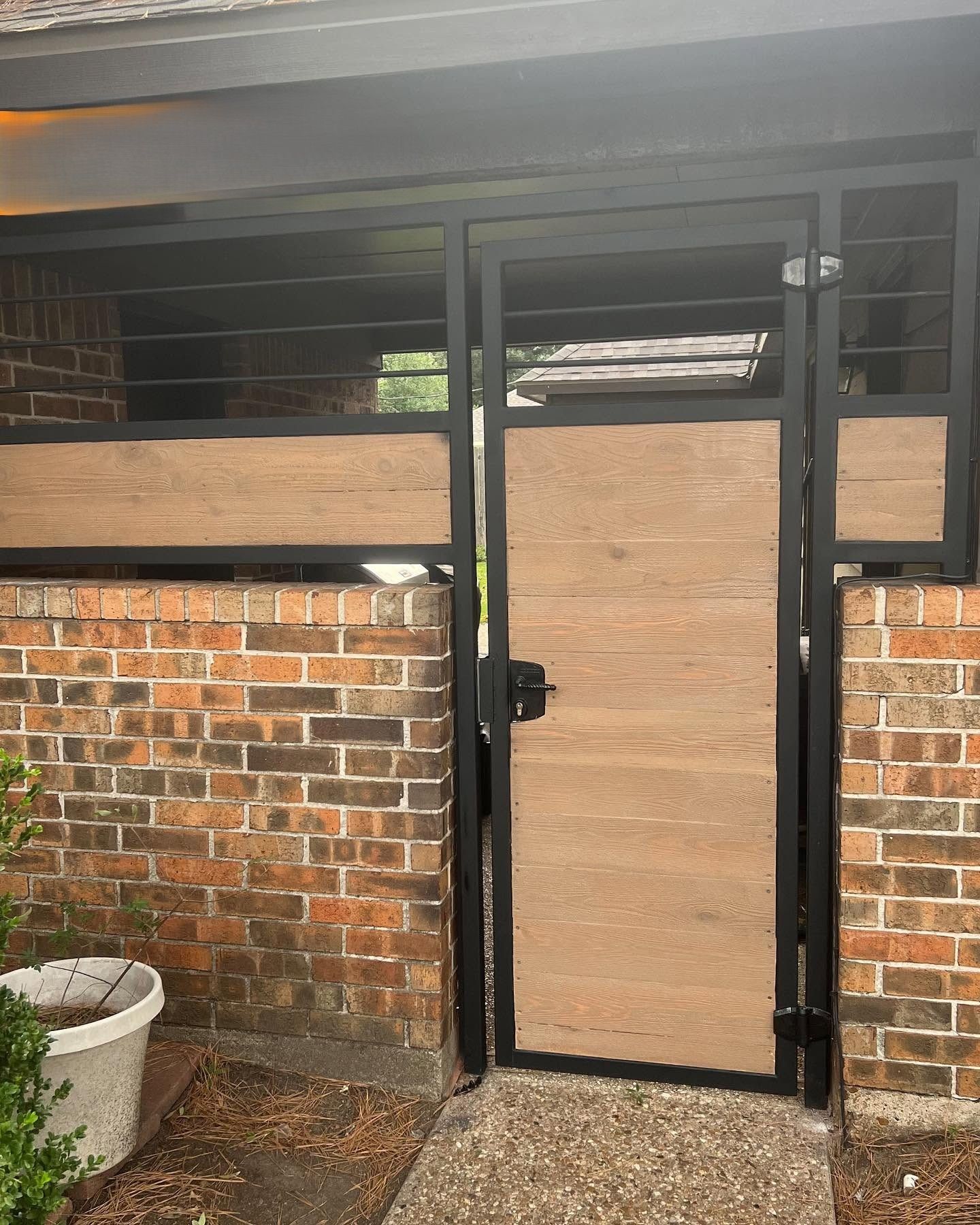 Brick entryway with black metal gate and boarded-up door under a porch roof.