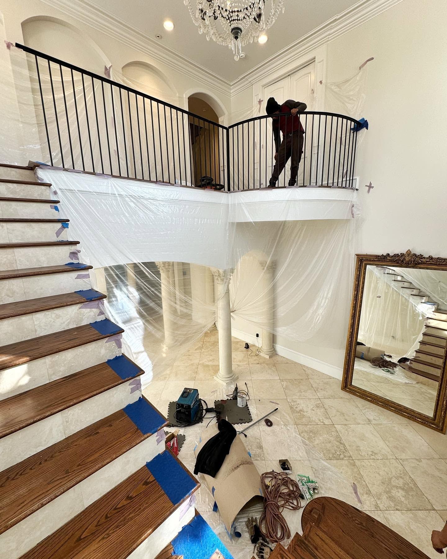 Grand foyer with curved staircase, chandelier, large mirror, and a person standing on the upstairs railing