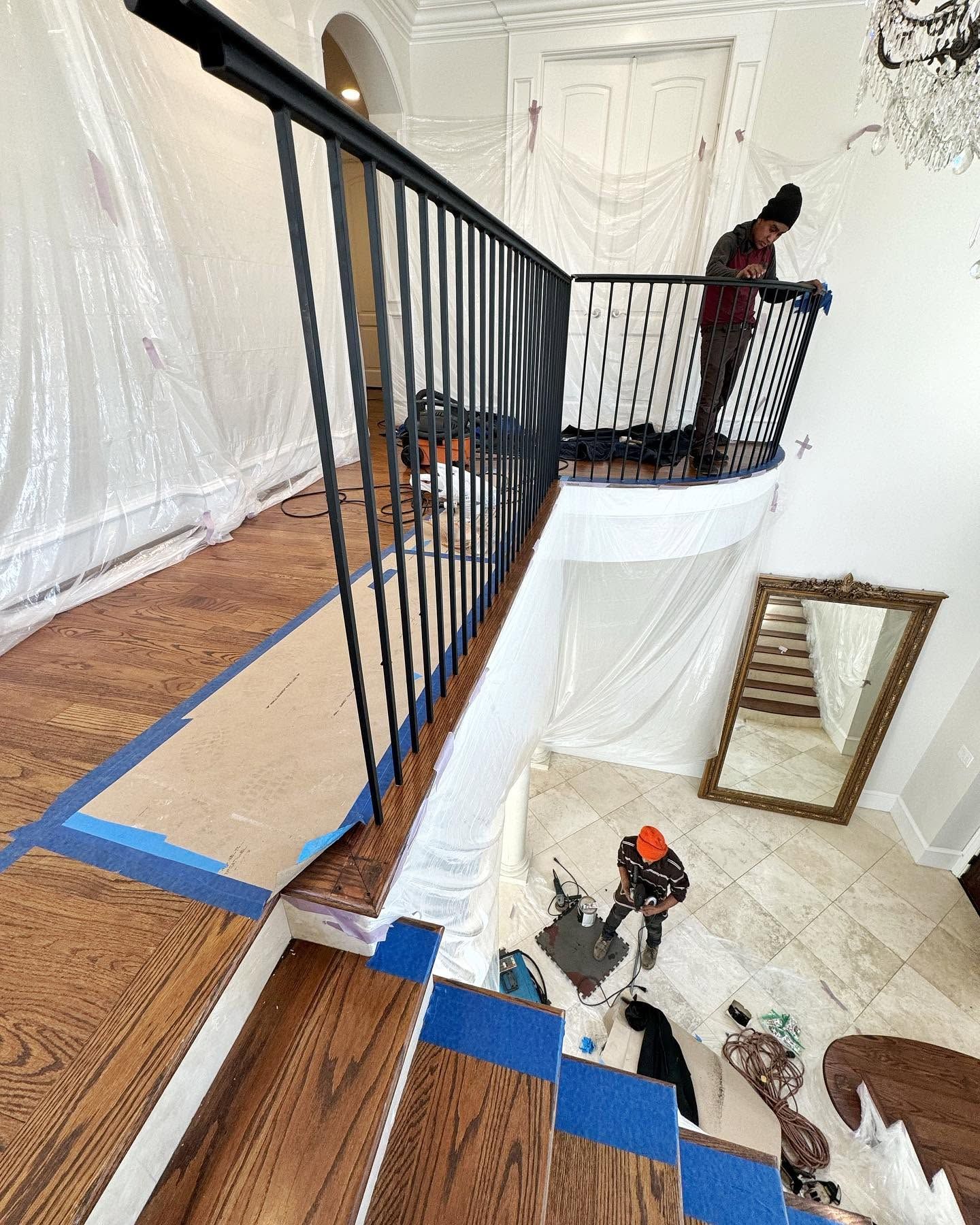 Stairway renovation with blue tape, black railing, and a worker on the upper landing.