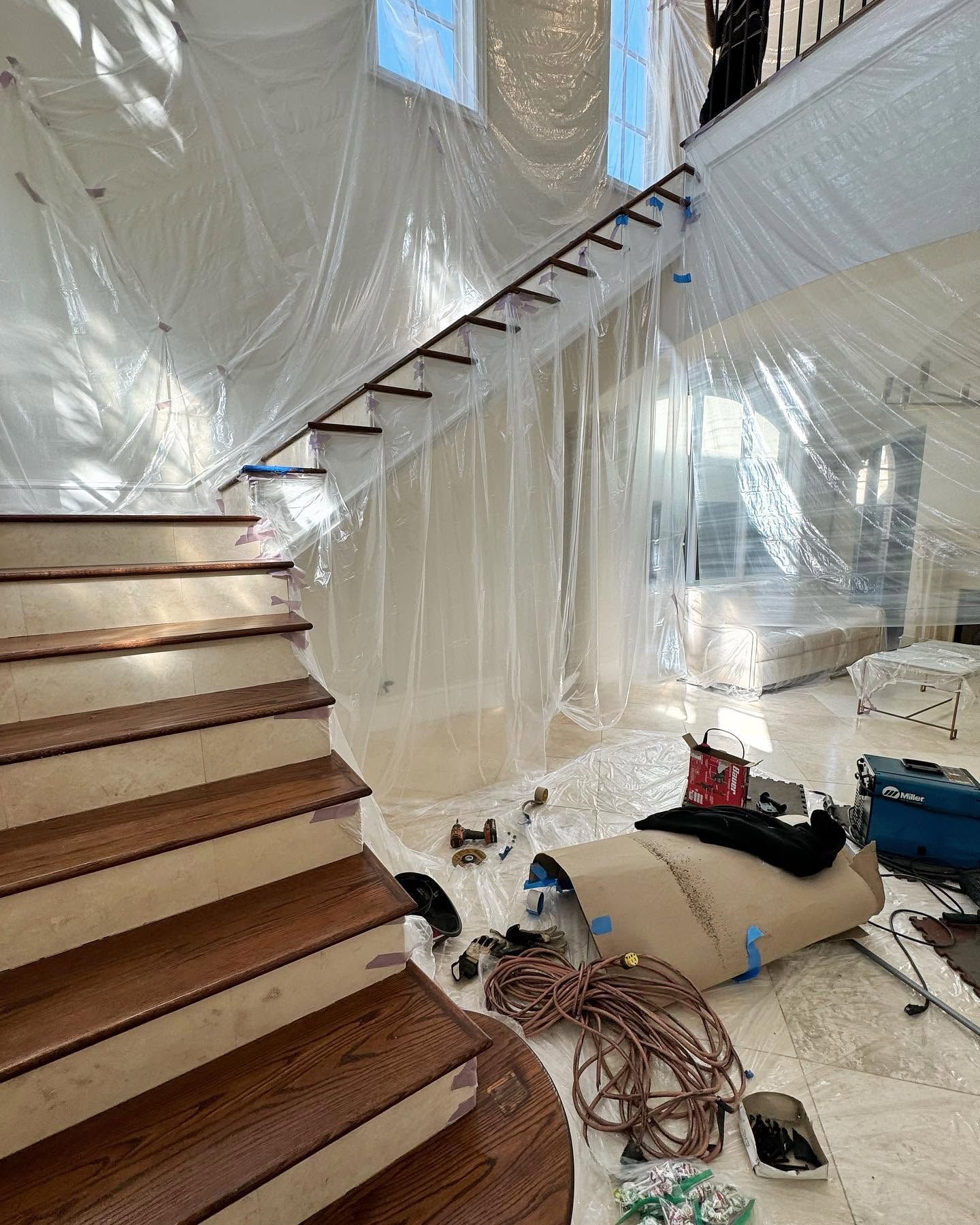 Plastic-covered staircase in a room under renovation, with tools and materials scattered on the floor.