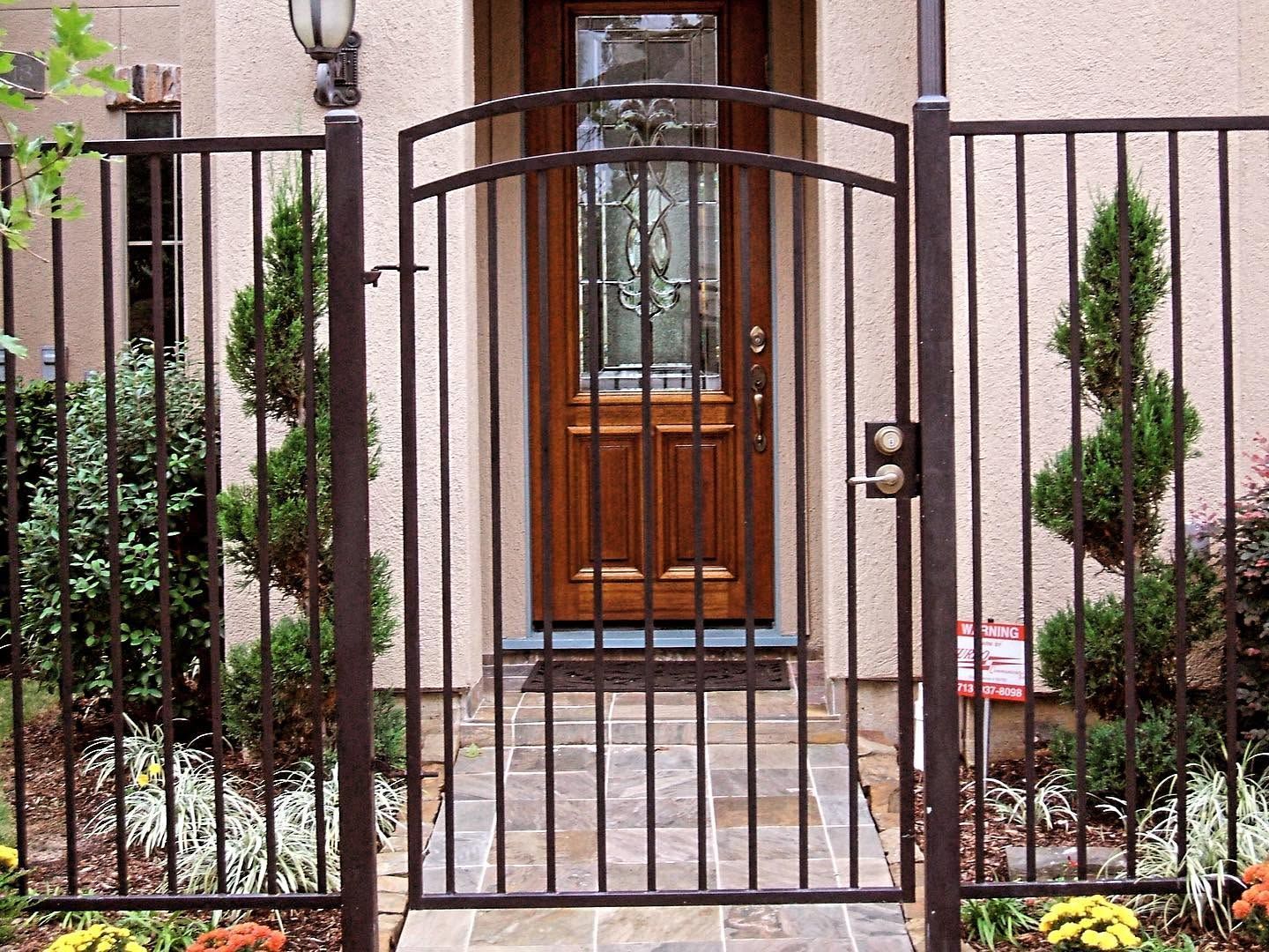 Wrought-iron gate in front of a house entrance with potted greenery on both sides