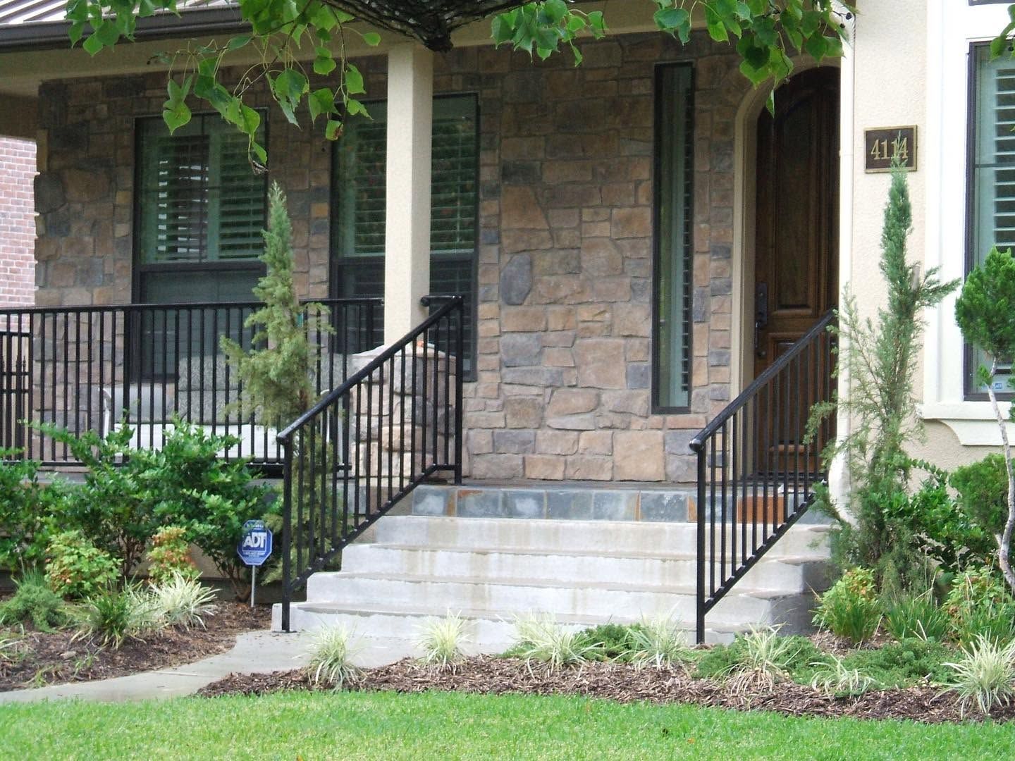 Front steps and porch of a brick house with black railings and stone facade
