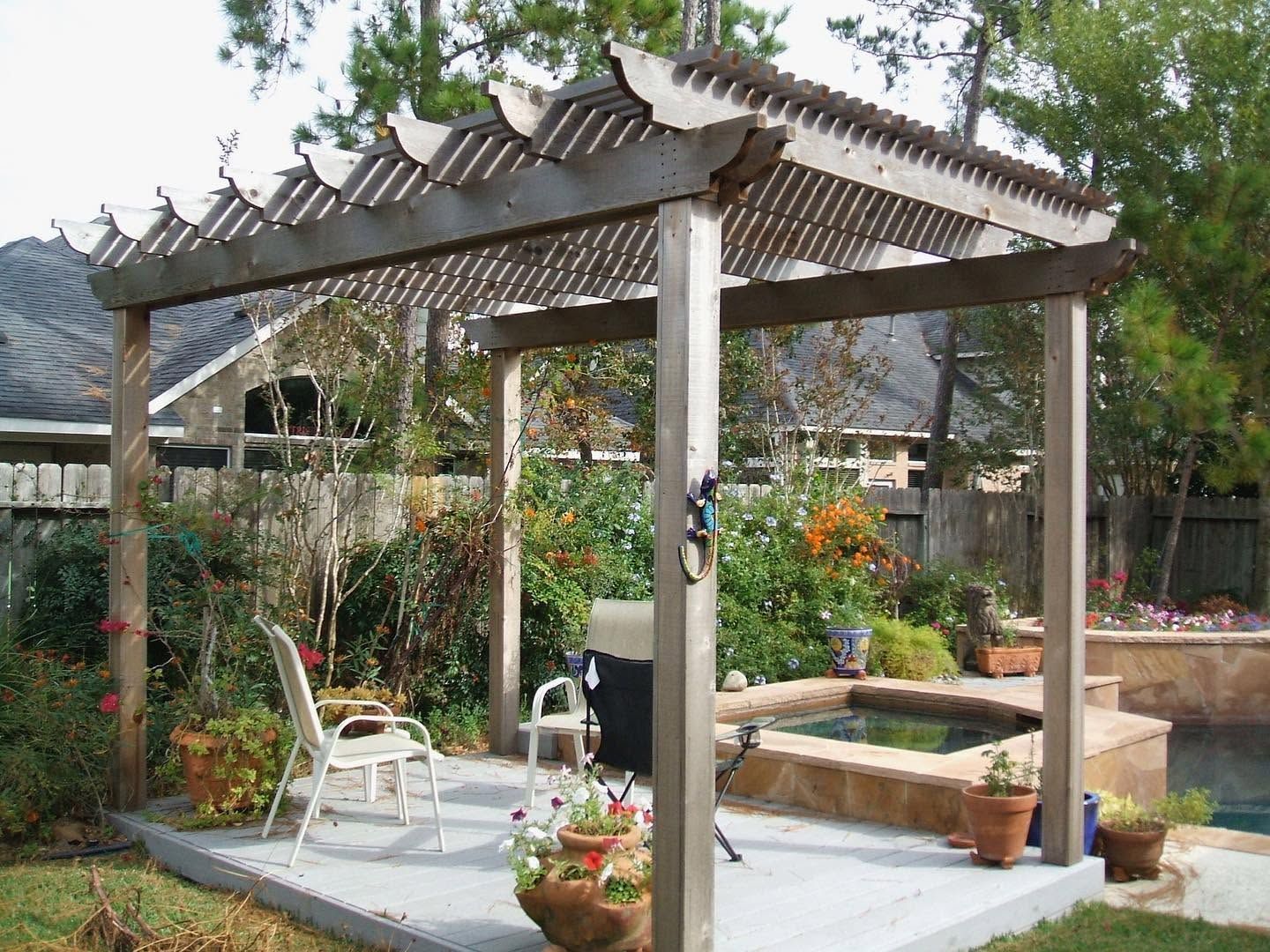 Backyard pergola with white chairs, potted flowers, and a small table in a garden setting