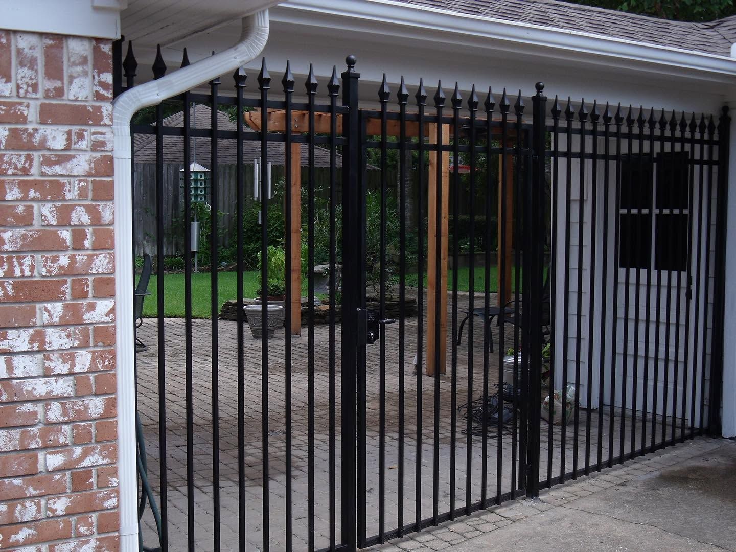 Black metal gate covering a carport beside a brick house, with driveway and yard beyond