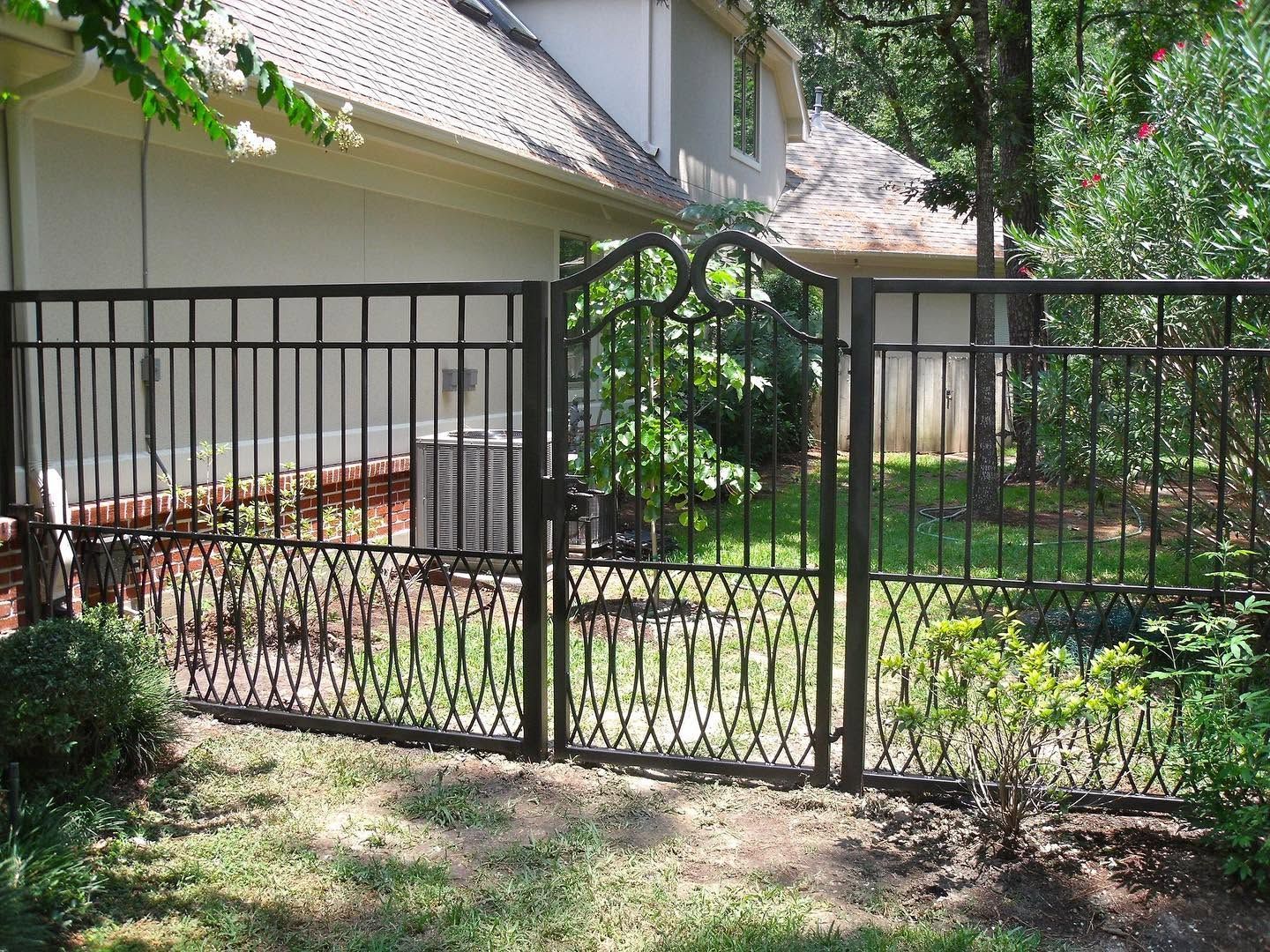 Black metal gate across a sunlit backyard with trees and a house in the background