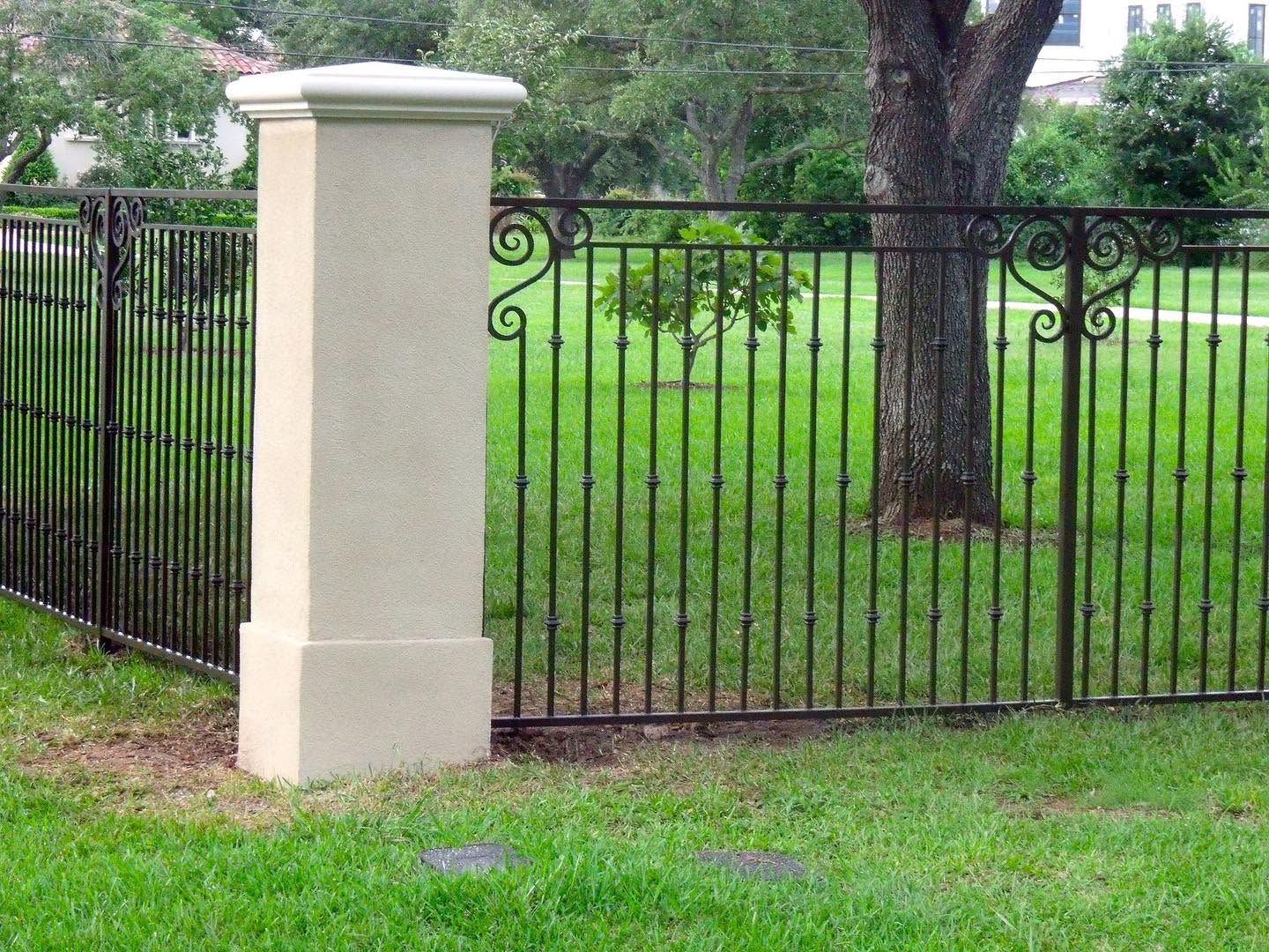 Black metal fence with a beige pillar beside a grassy yard and trees