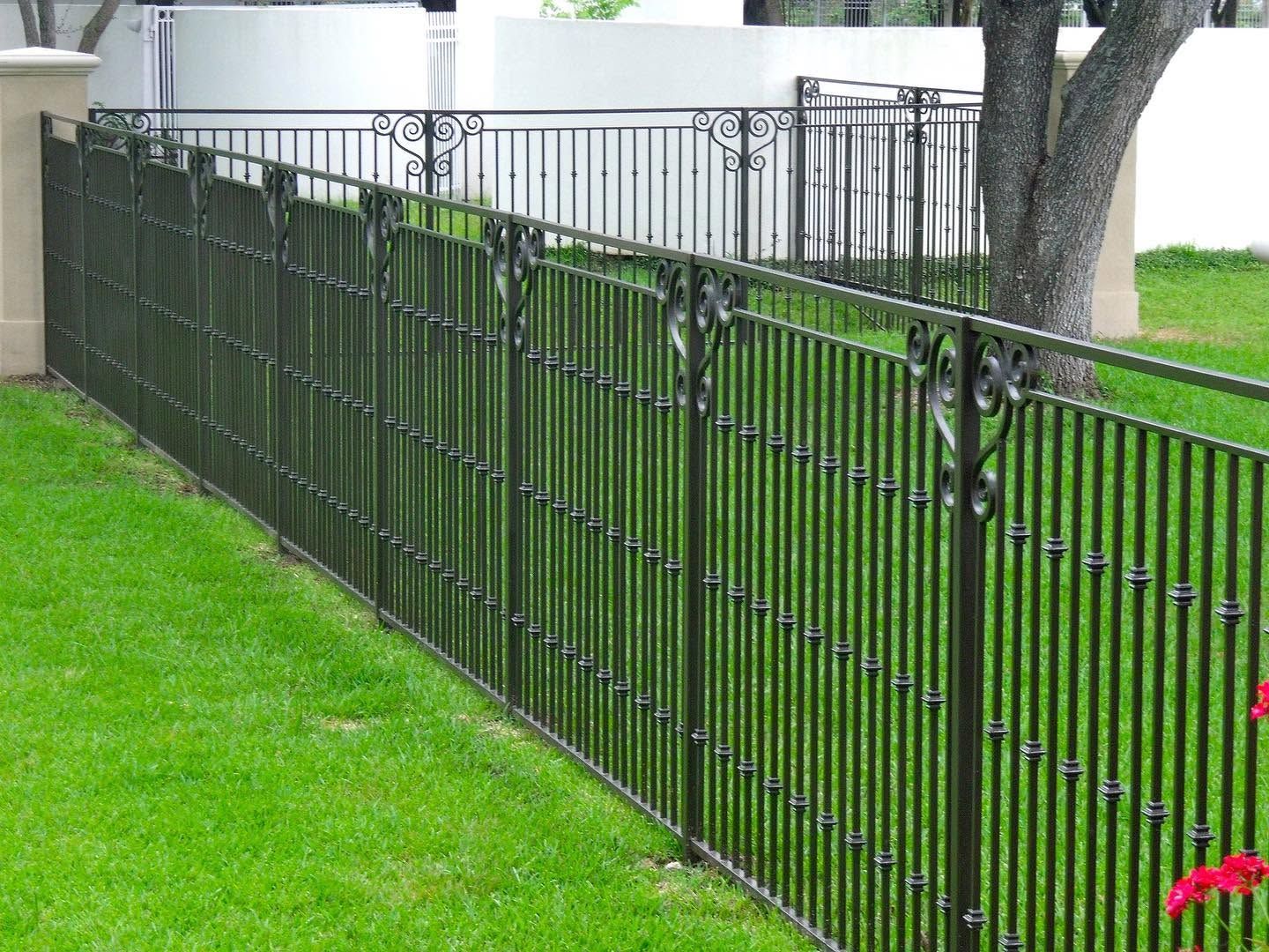 Black metal fence along a grassy slope beside a walkway and tree