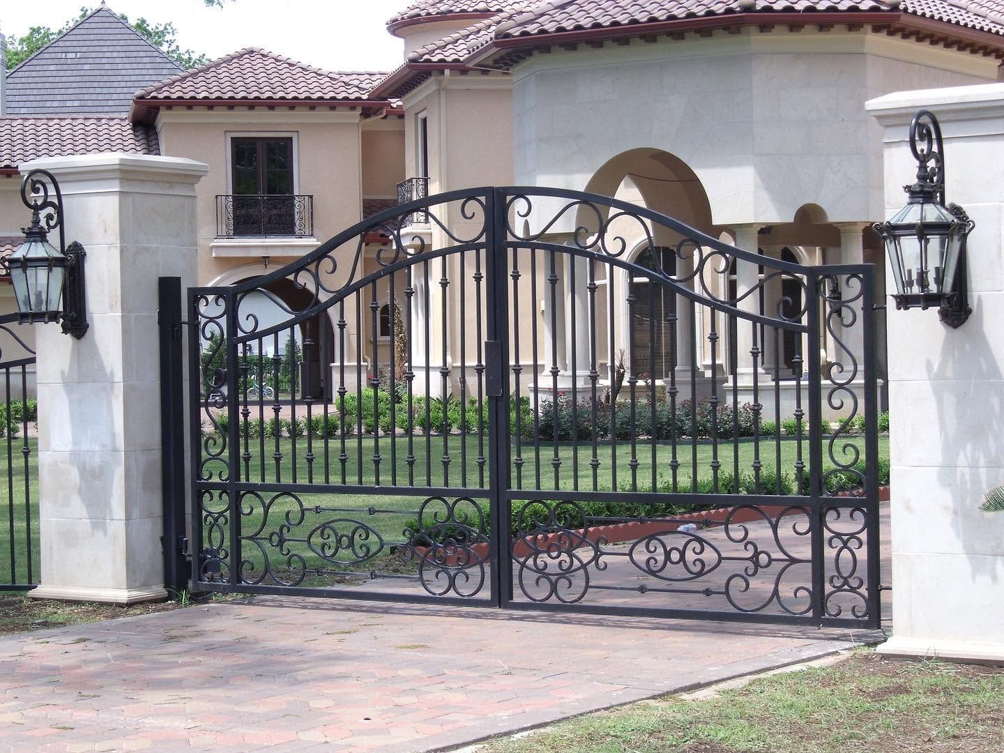 Black wrought-iron gate in front of a white stucco house with a tiled roof and arched entryway