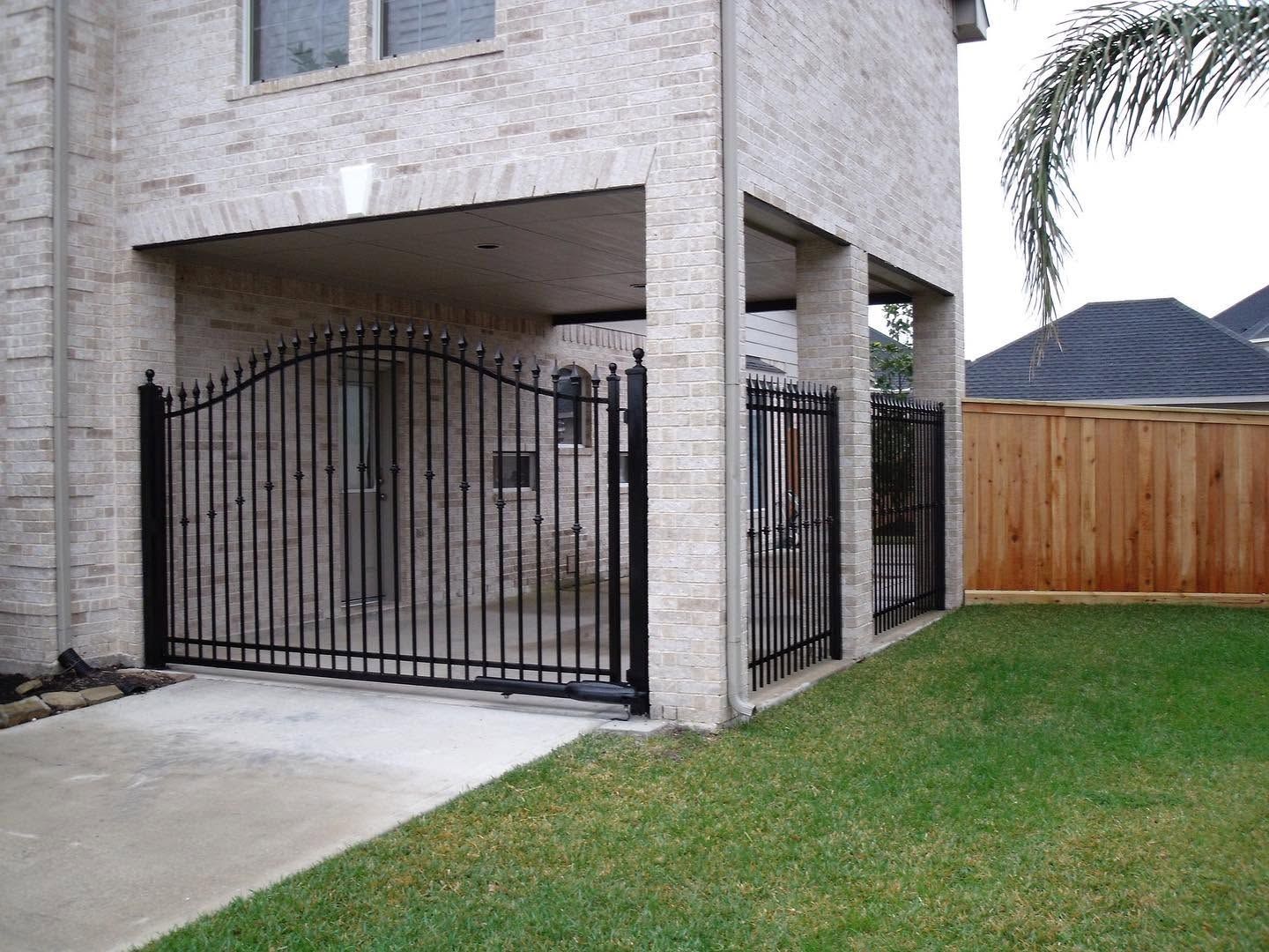 Black metal gate across a concrete driveway beside a beige house and green lawn