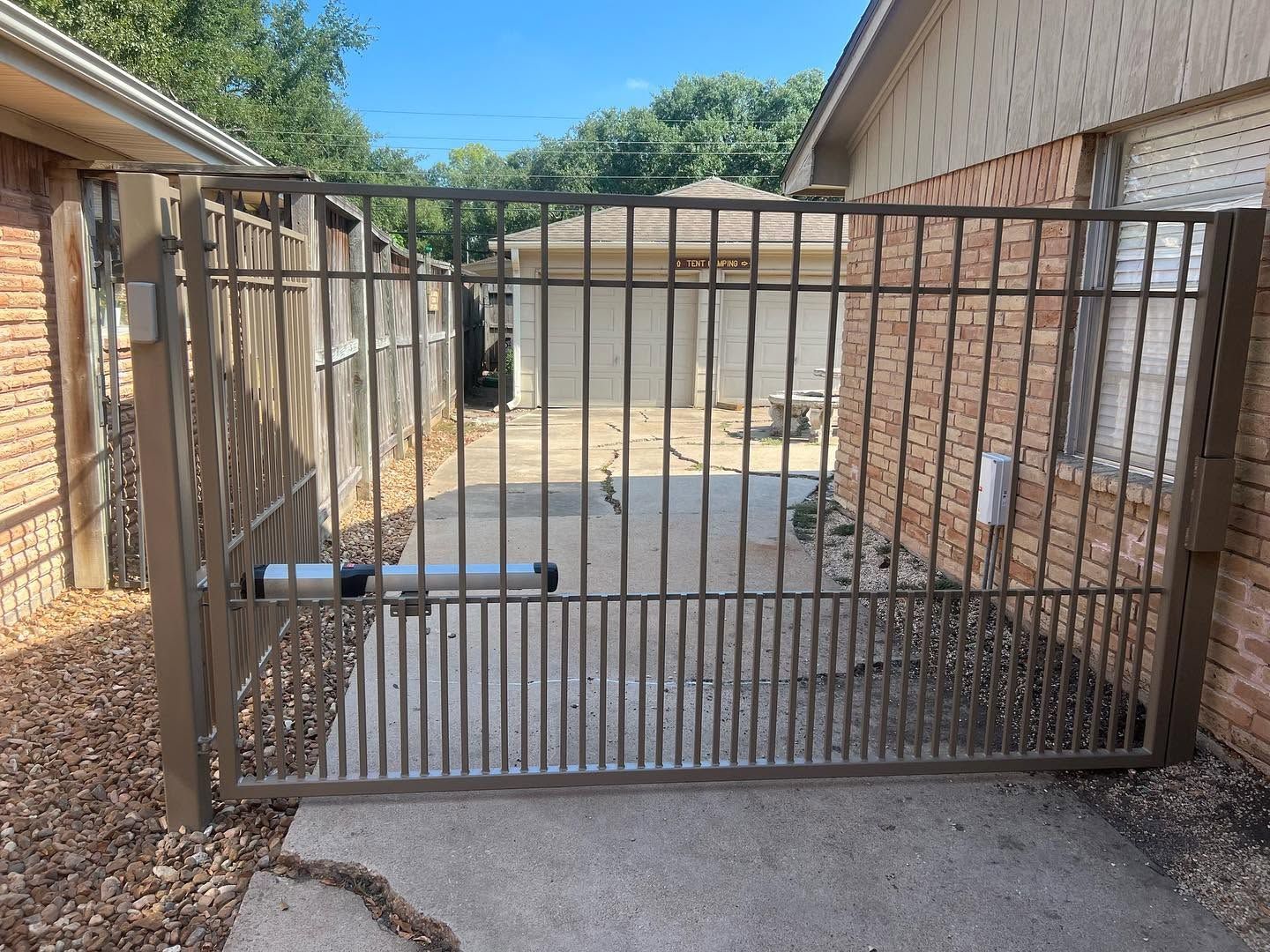 Closed metal driveway gate between brick walls in a sunlit driveway