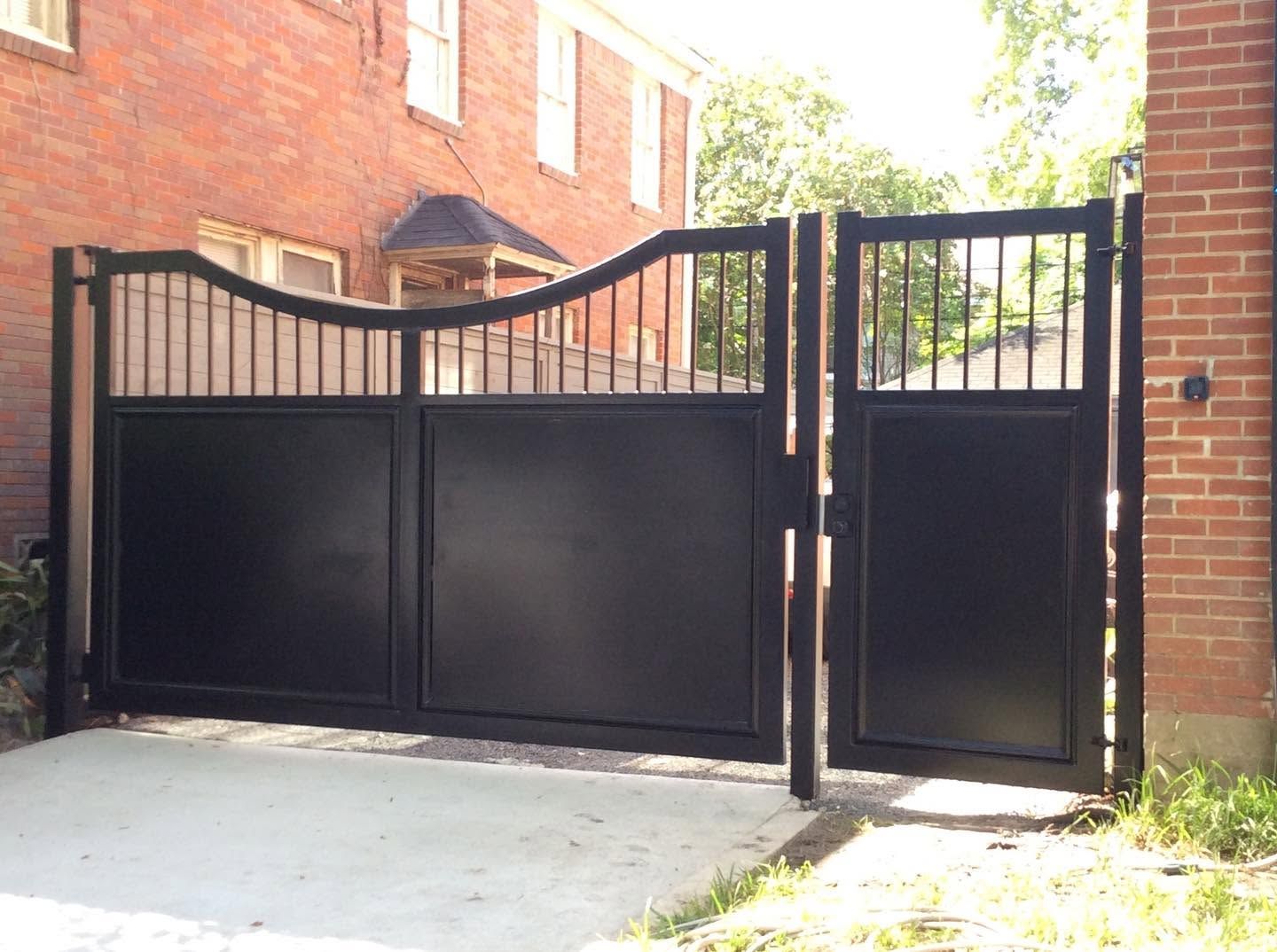 Black metal driveway gate beside a brick building and sidewalk, with a matching pedestrian gate.