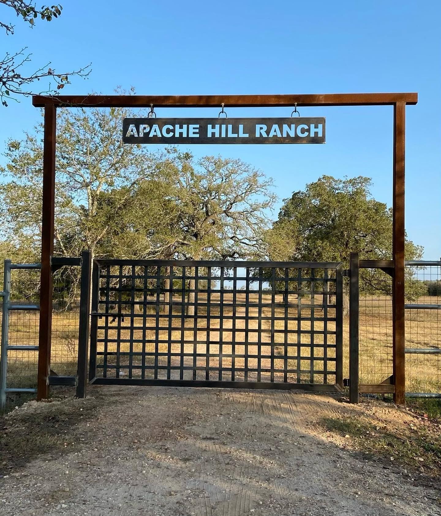 Gated ranch entrance with sign reading “APACHE HILL RANCH” under a clear blue sky.
