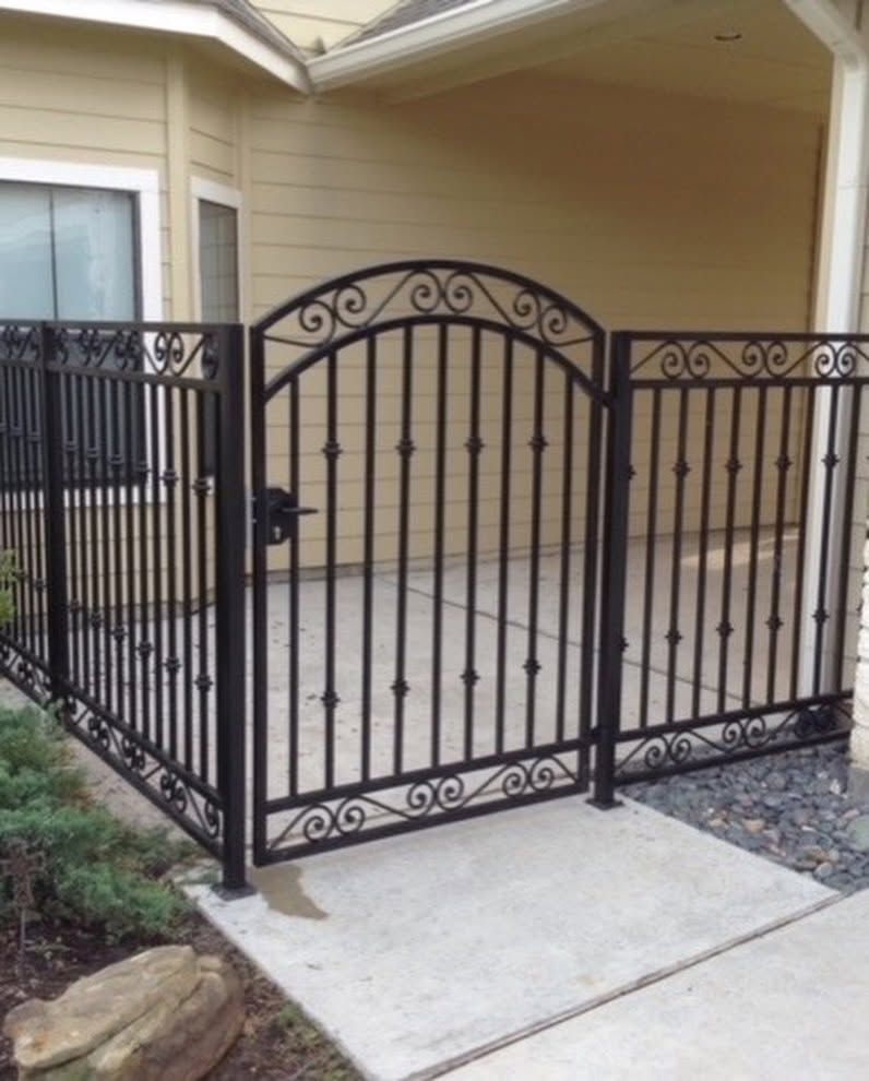 Black wrought-iron fence and gate enclosing a small concrete patio outside a beige house.