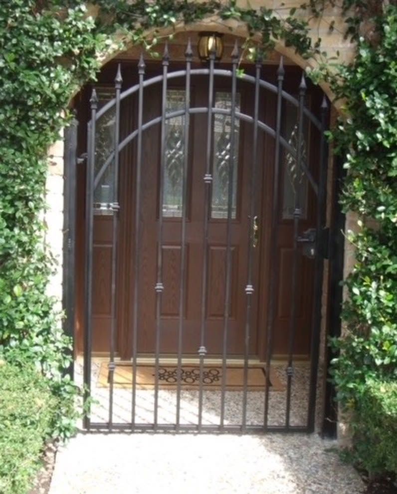 Black iron gate in a vine-covered stone archway, blocking a wooden front door.