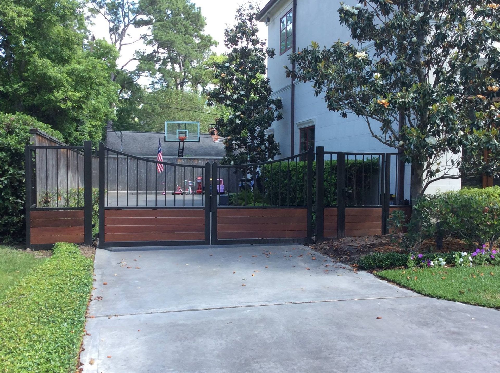 Gated driveway leading to a house, with a basketball hoop and trees along the entrance.