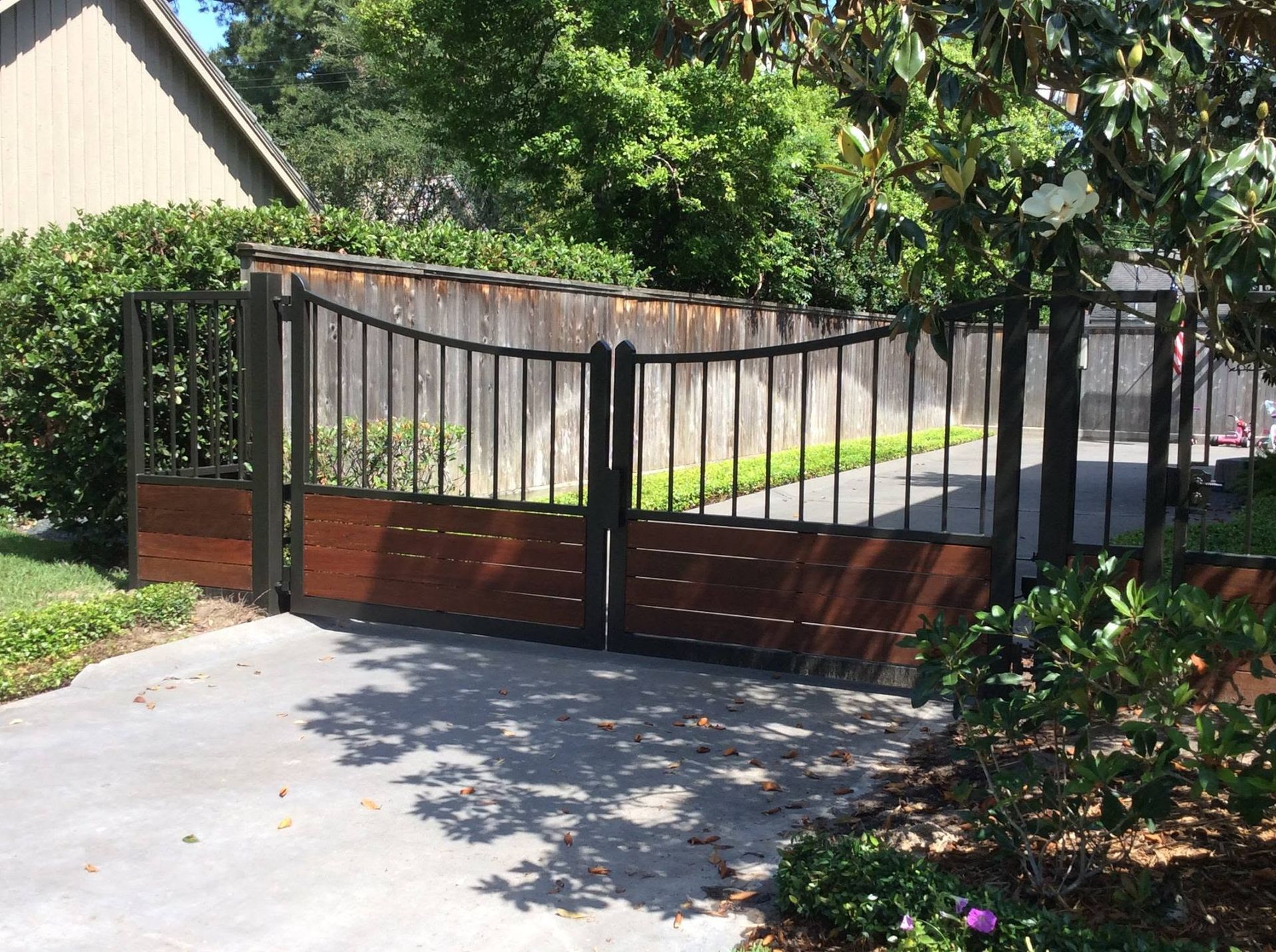 Black metal driveway gate with brick base at the entrance to a suburban home.