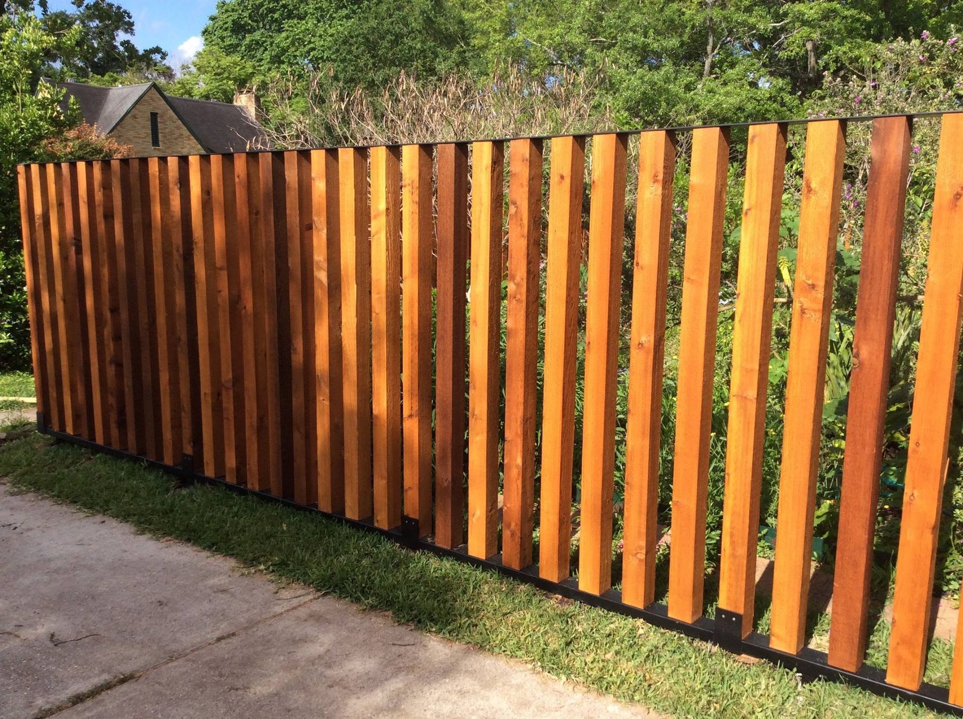 Wooden slat fence with orange-brown vertical boards beside a sidewalk and greenery