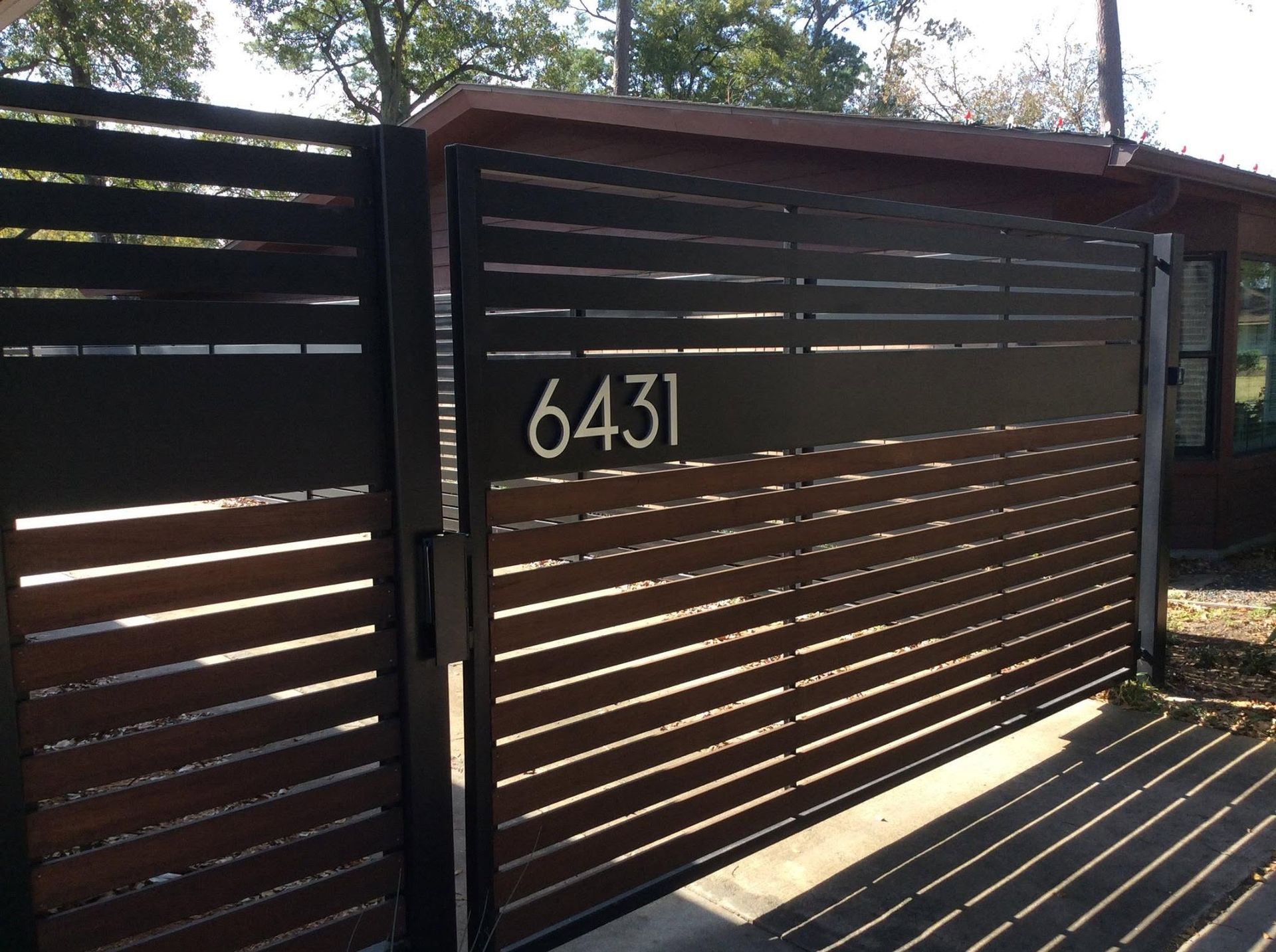 Dark wooden slatted gate with house number 6431 in sunlight
