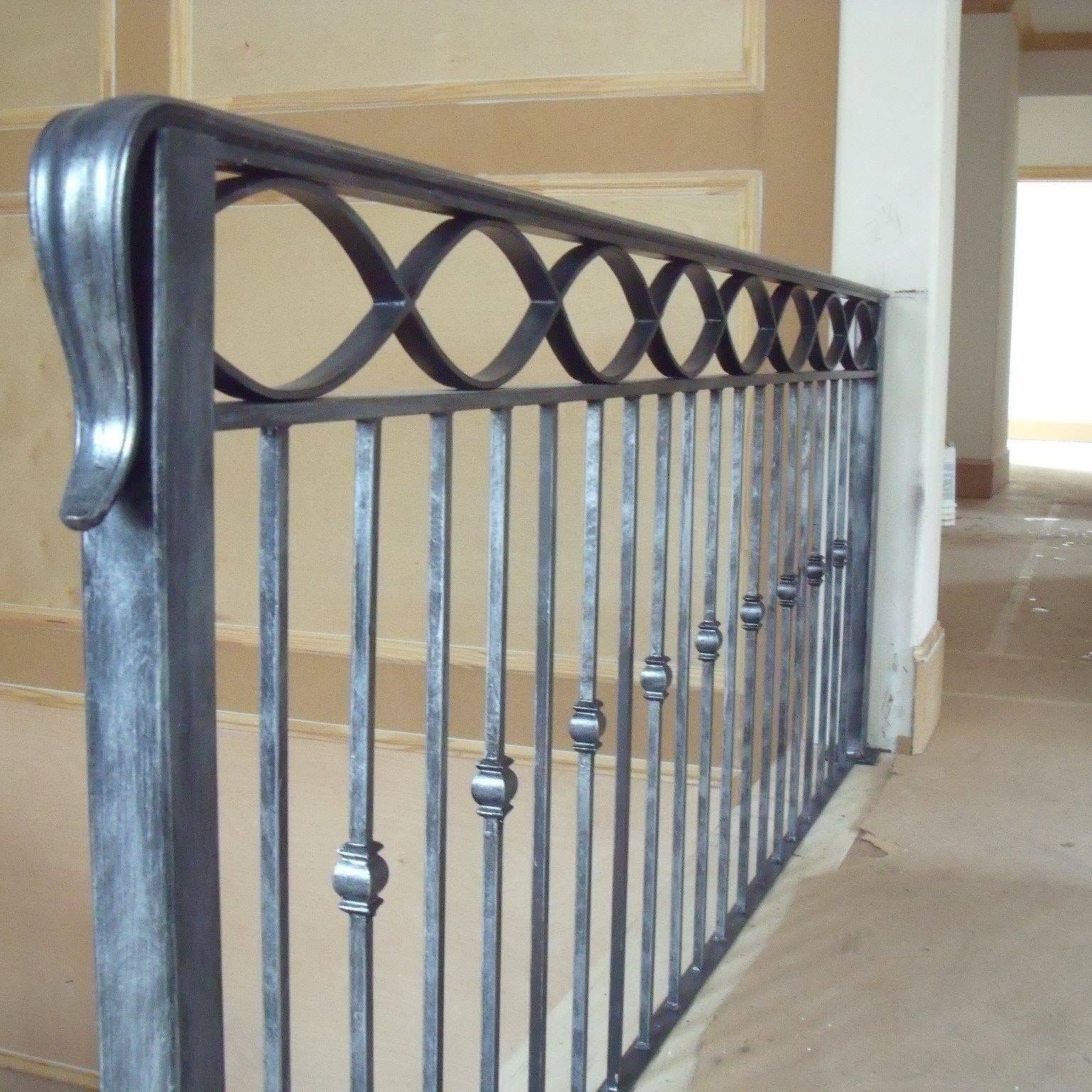 Black wrought-iron stair railing with decorative loops along a carpeted hallway.