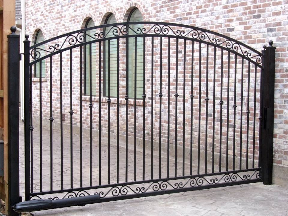 Black wrought-iron driveway gate in front of a brick wall