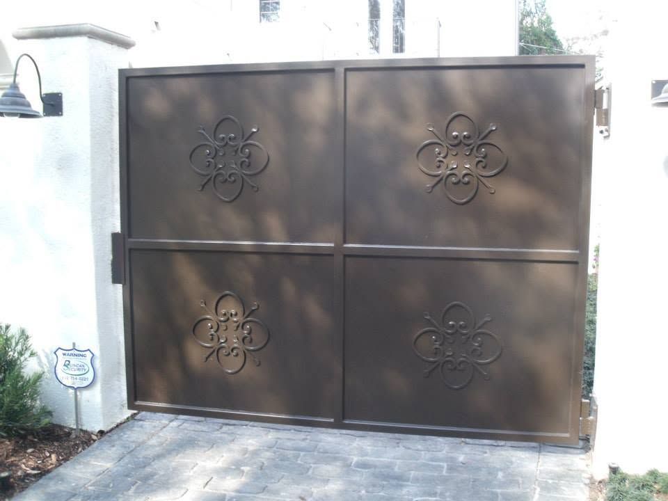 Brown metal driveway gate with decorative floral designs in front of a house