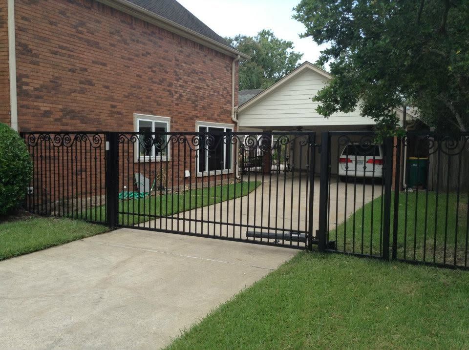 Black metal driveway gate across a suburban brick house driveway and lawn.