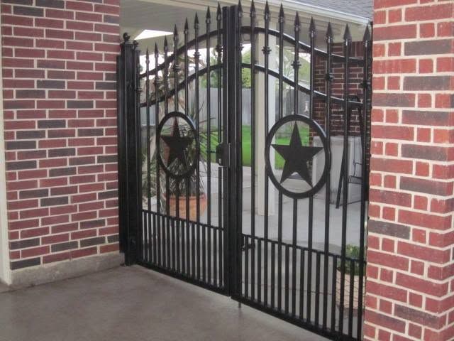 Black wrought-iron gate with star designs between red brick pillars at a driveway entrance