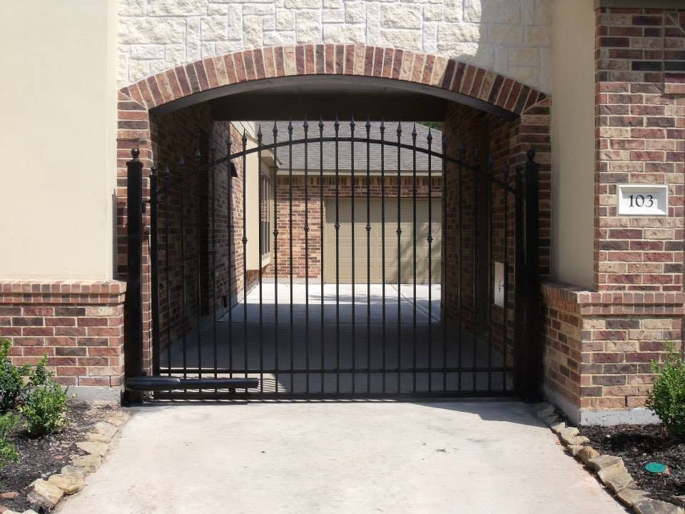Black iron gate in a brick archway entrance to a building courtyard