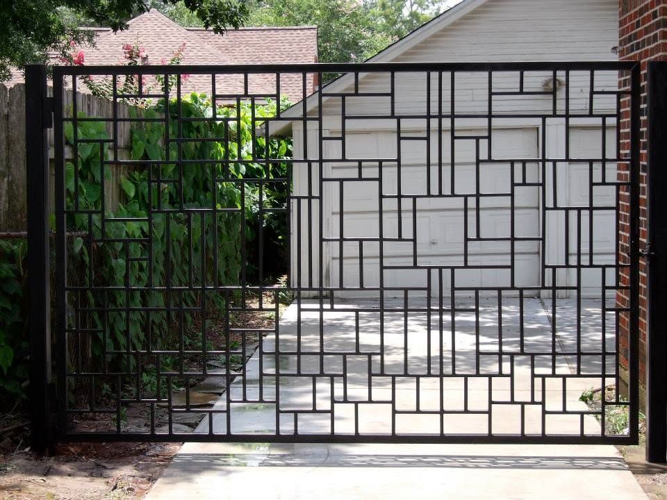 Black metal gate in front of a white garage with a stone-pattern wall and driveway.