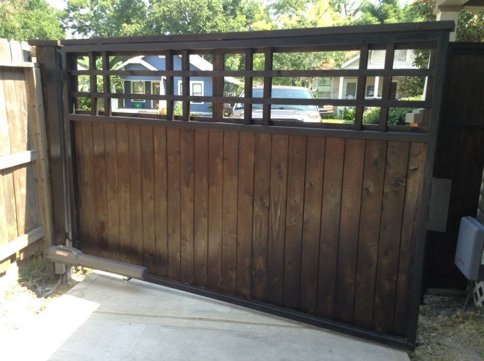 Wooden driveway gate with black metal frame and narrow top windows beside a concrete path