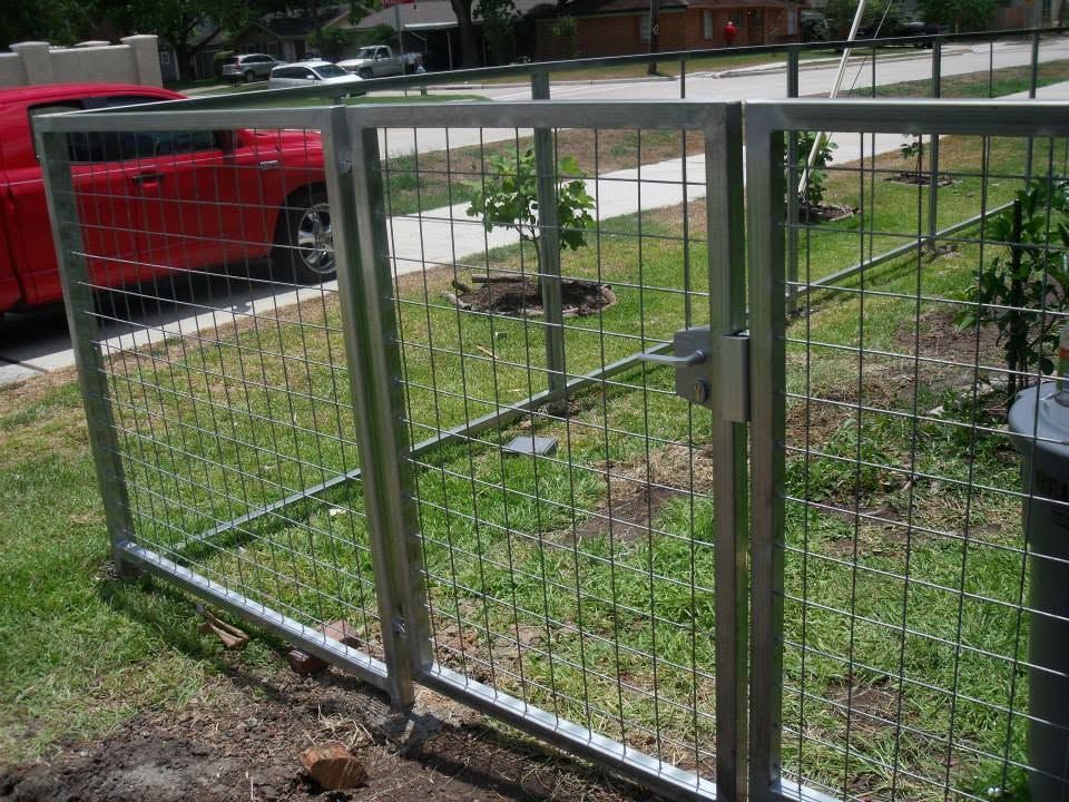 Metal fence gate in a grassy yard beside a red truck and sidewalk