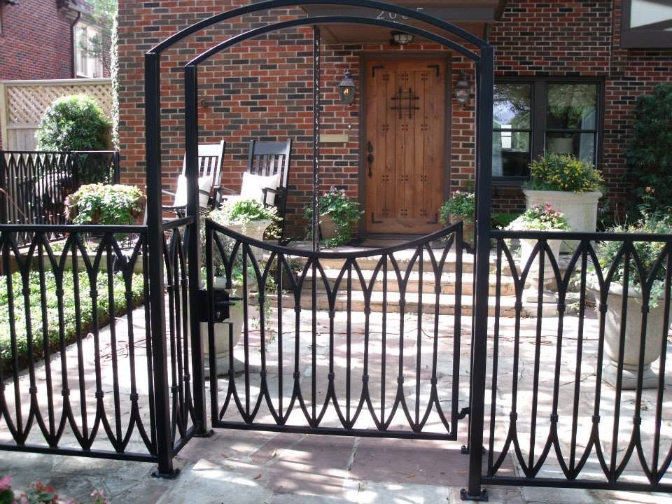 Black metal garden gate before a brick house with a wooden door and potted plants