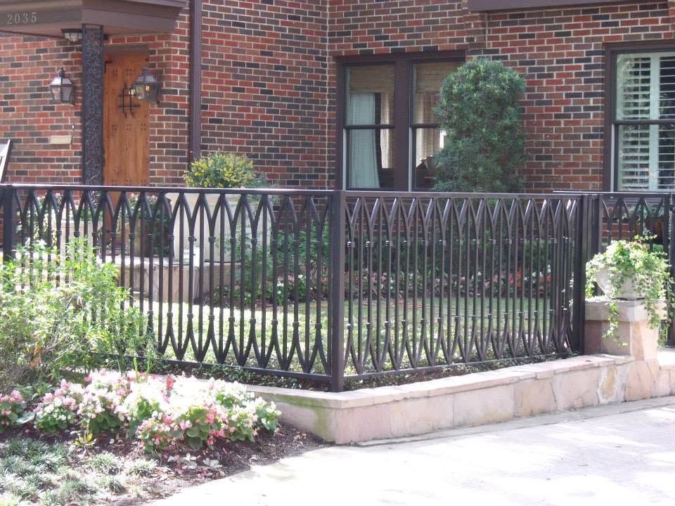Black metal railing around a brick townhouse patio with shrubs and flower beds