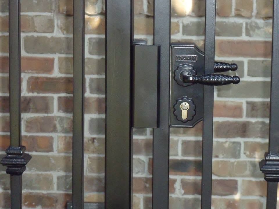 Black metal gate with a keypad lock and handle against a brick wall.