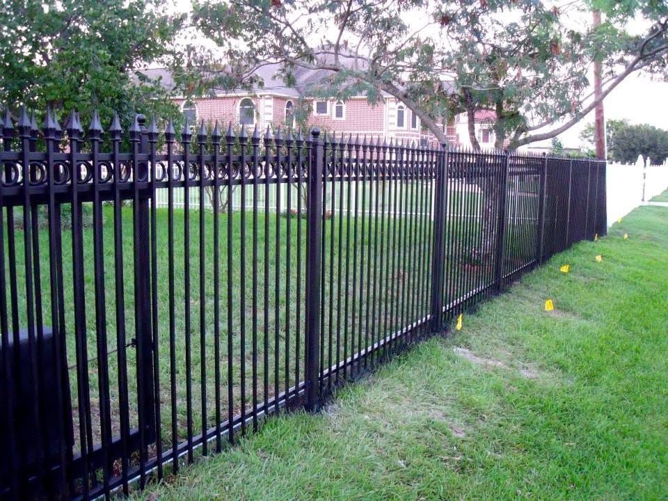 Black metal fence along a grassy yard beside houses and trees