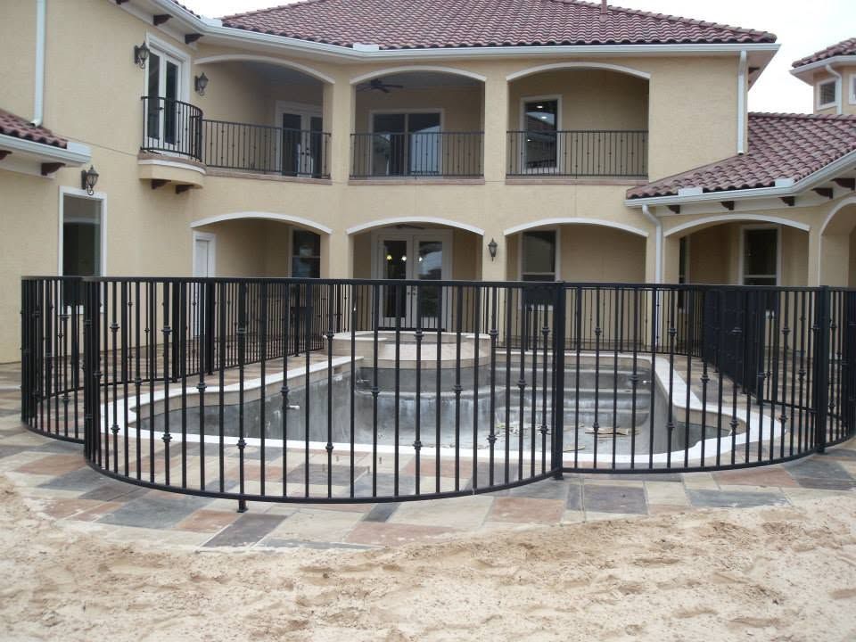 Black metal fence around a circular fountain in a courtyard before a beige villa