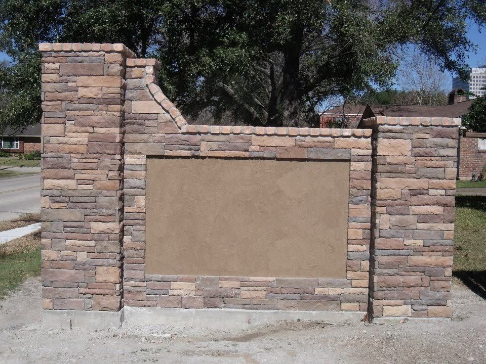 Stone community sign with blank tan center panel beside a sidewalk and trees
