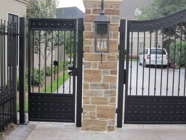 Black metal gates with a stone pillar and lantern at a driveway entrance.