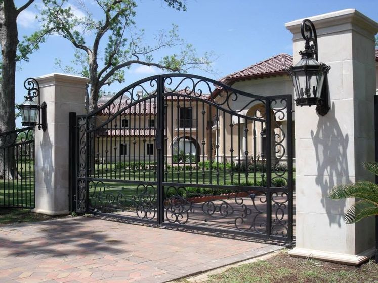 Black wrought-iron driveway gate between white stucco pillars at a Mediterranean-style house