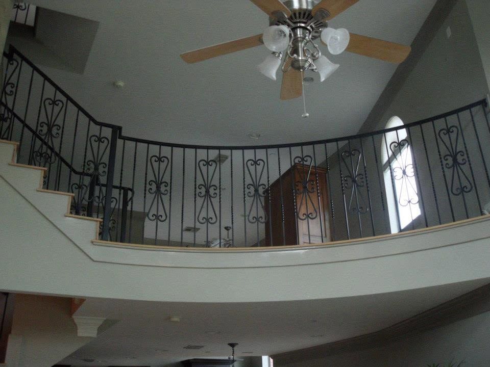 Interior view of a two-story foyer with curved balcony, black iron railing, and ceiling fan