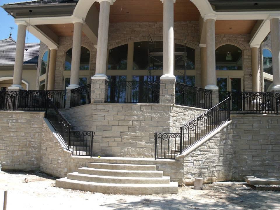 Stone building entrance with columns, steps, and black railings under a covered porch
