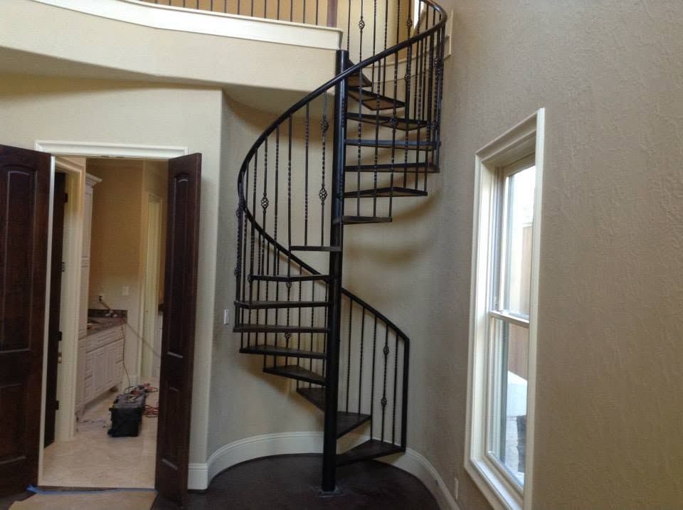 Curved black spiral staircase in a beige foyer with white trim and a window.