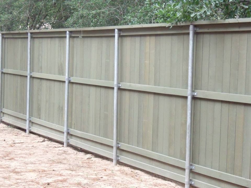 Wooden privacy fence with gray metal posts along a dirt path, backed by trees