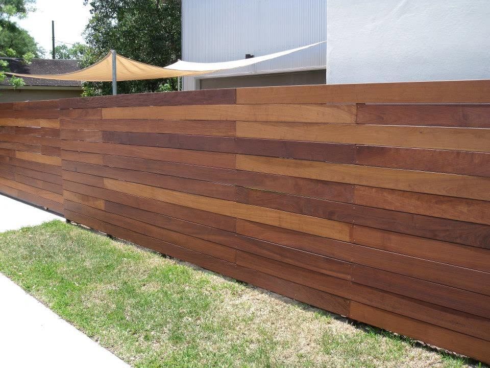 Wooden slat fence beside a grassy sidewalk outside a modern building