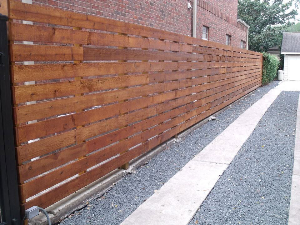 Long wooden fence beside a narrow gravel path next to a brick building