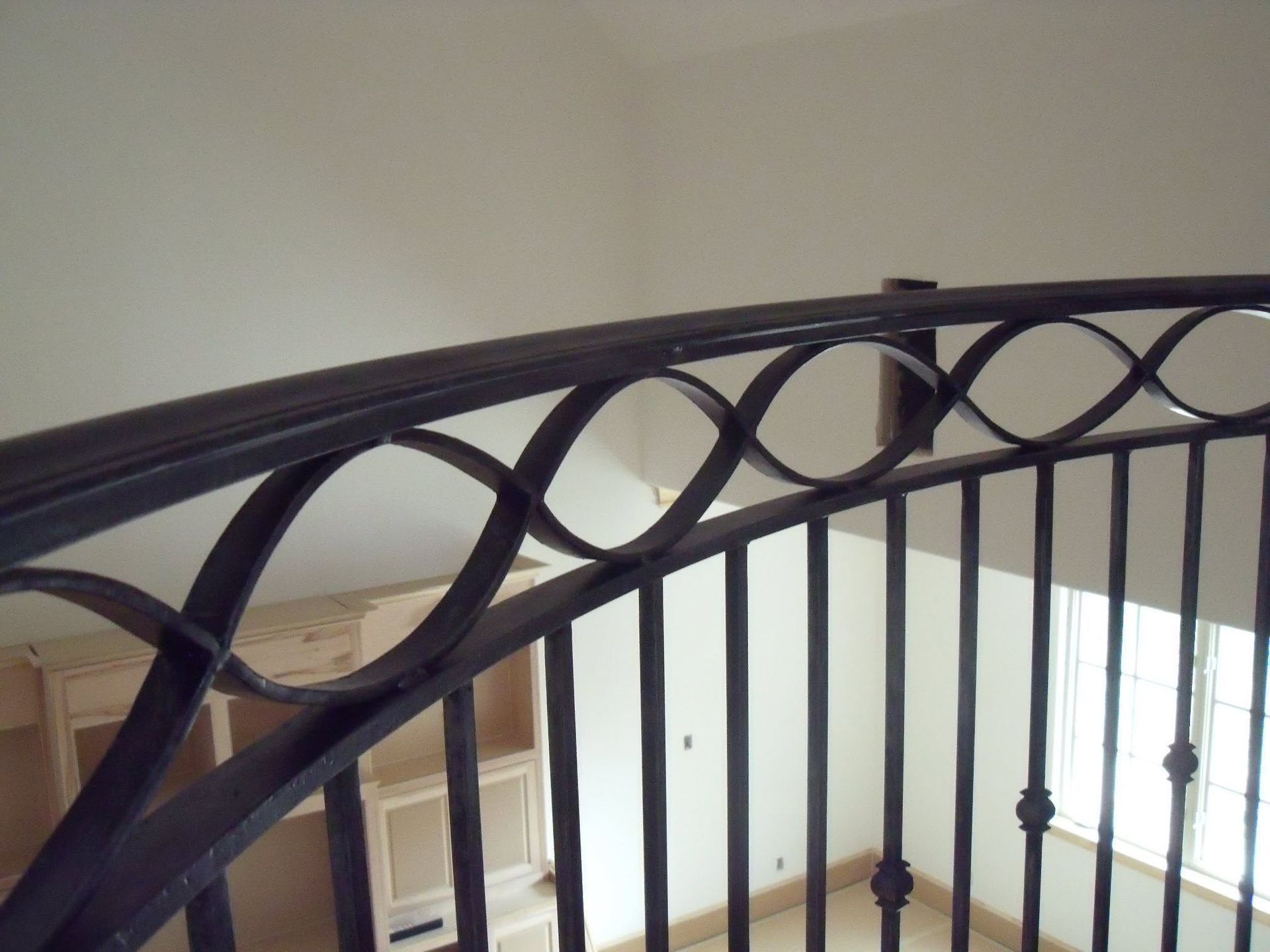 Black metal staircase railing with oval scrollwork in an indoor hallway.